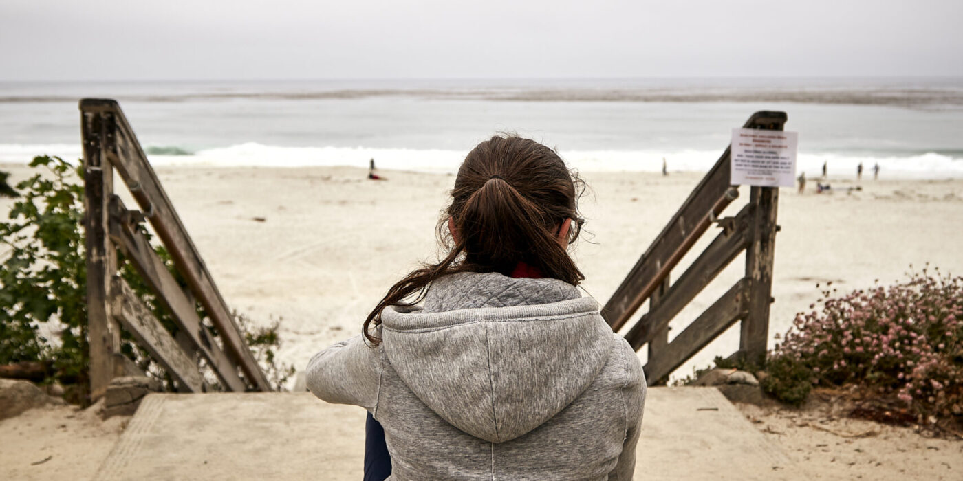 Adolescente sentada sozinha de costas em uma praia em dia nublado