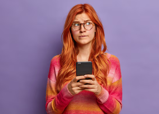 Mulher de óculos olhando para o celular com expressão desconfiada